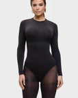 Woman wearing a black bodysuit with sheer panels on a white background