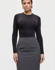 Woman wearing a black long-sleeve top and gray skirt on a white background