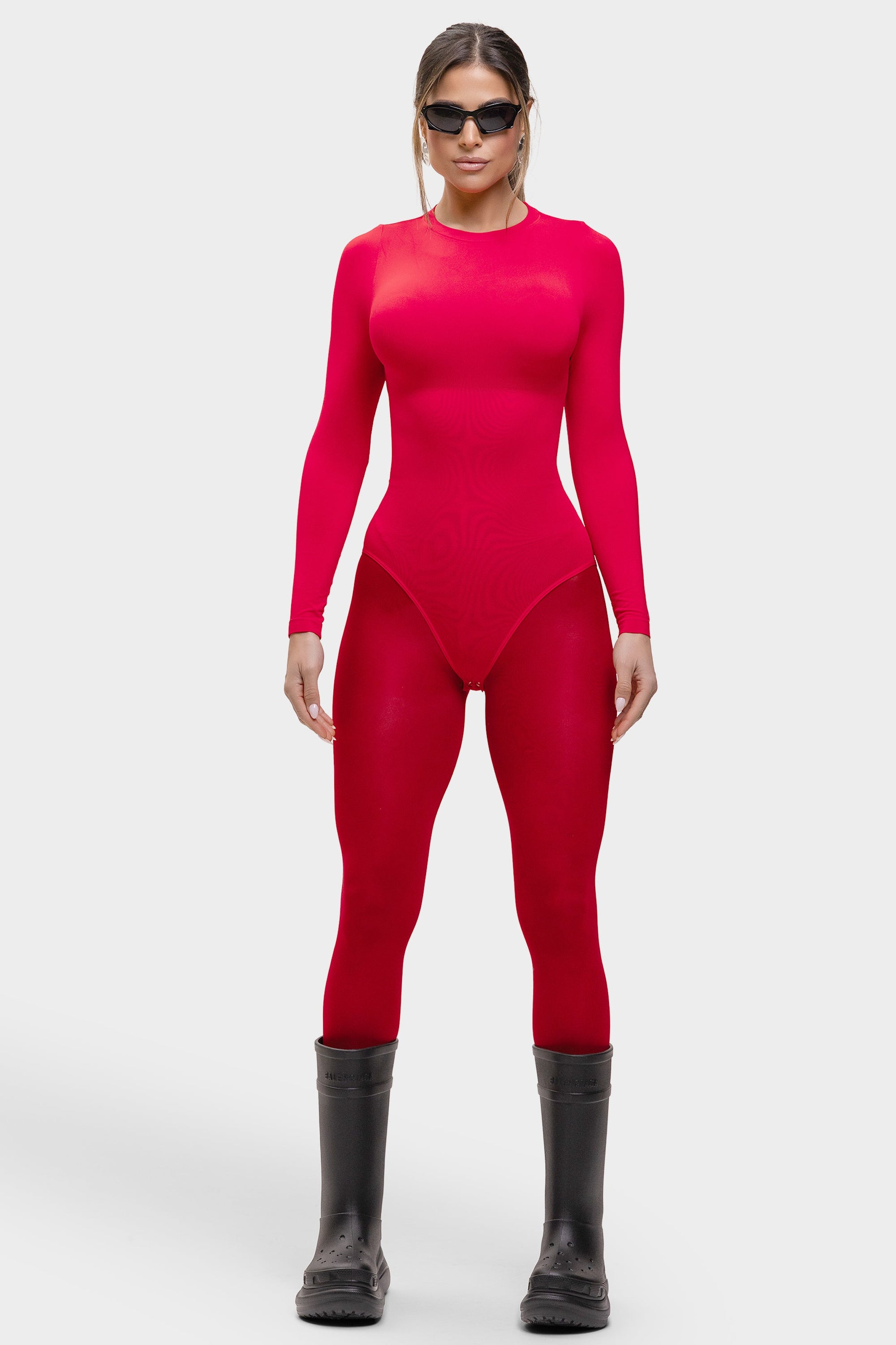 Person wearing a bright red bodysuit and black boots on a white background