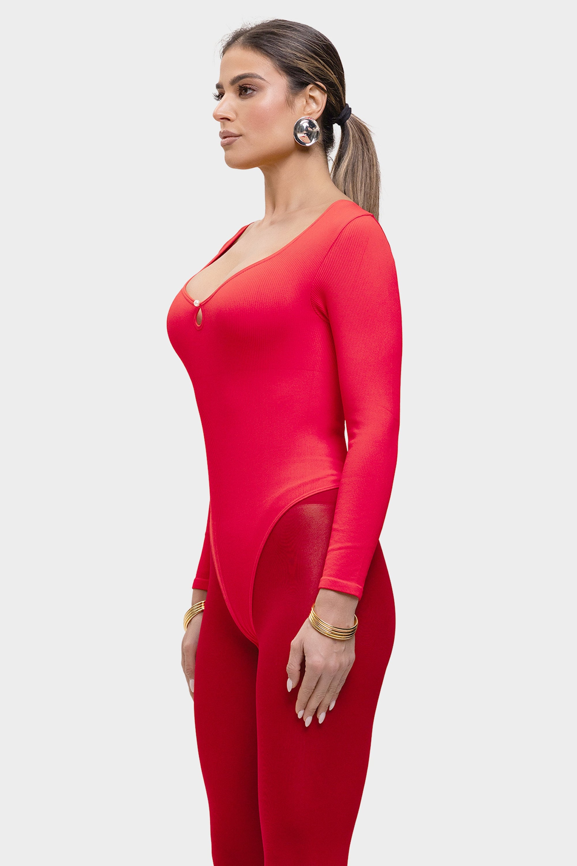 Woman wearing a red outfit with a plunging neckline and long sleeves on a white background