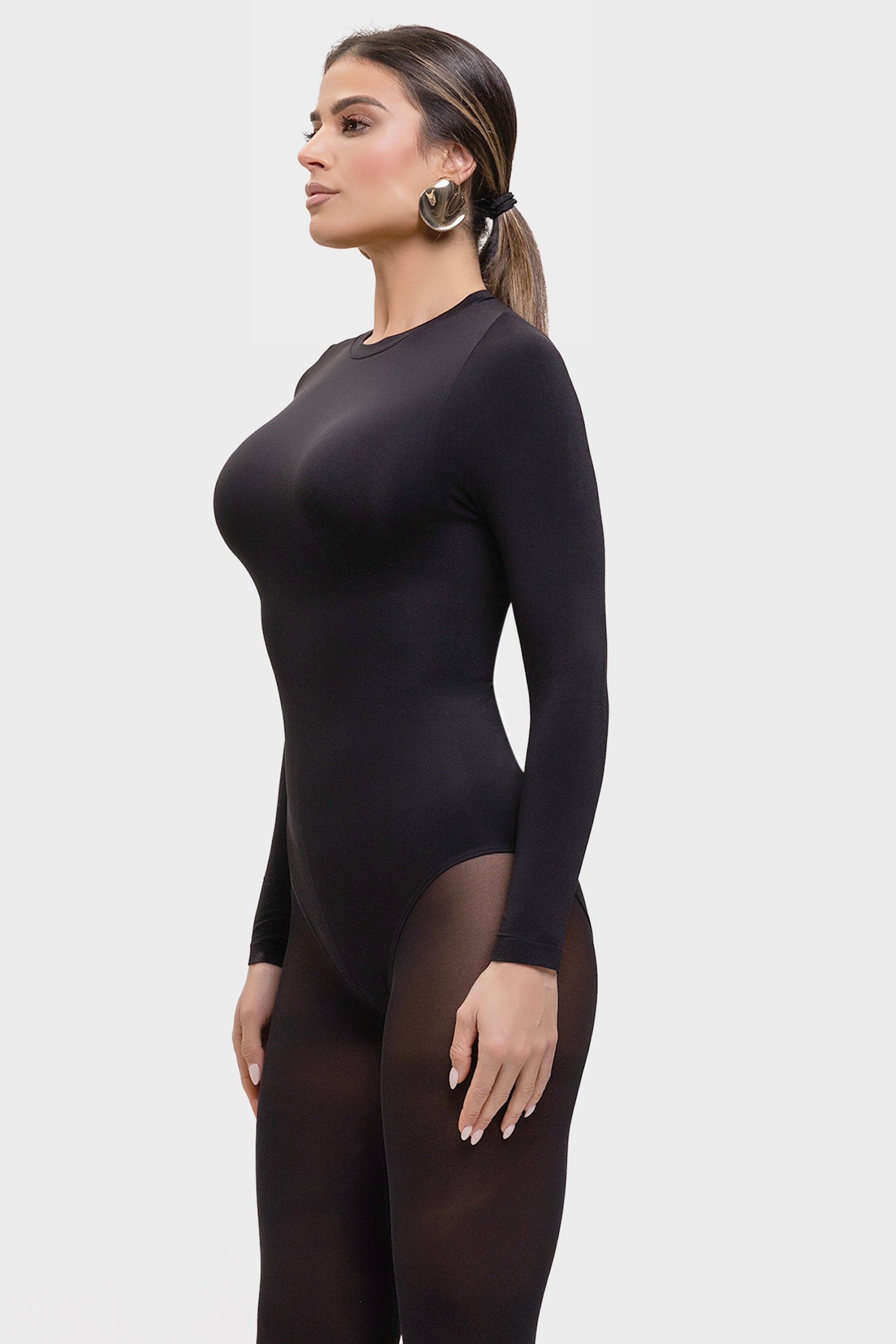 Woman wearing a black bodysuit with sheer panels on a white background