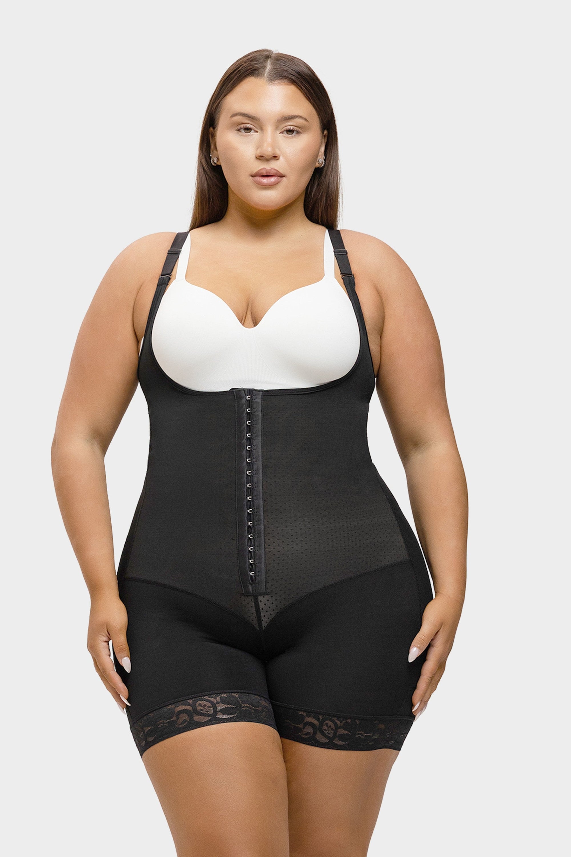 Woman wearing a black shapewear garment over a white bra on a plain background