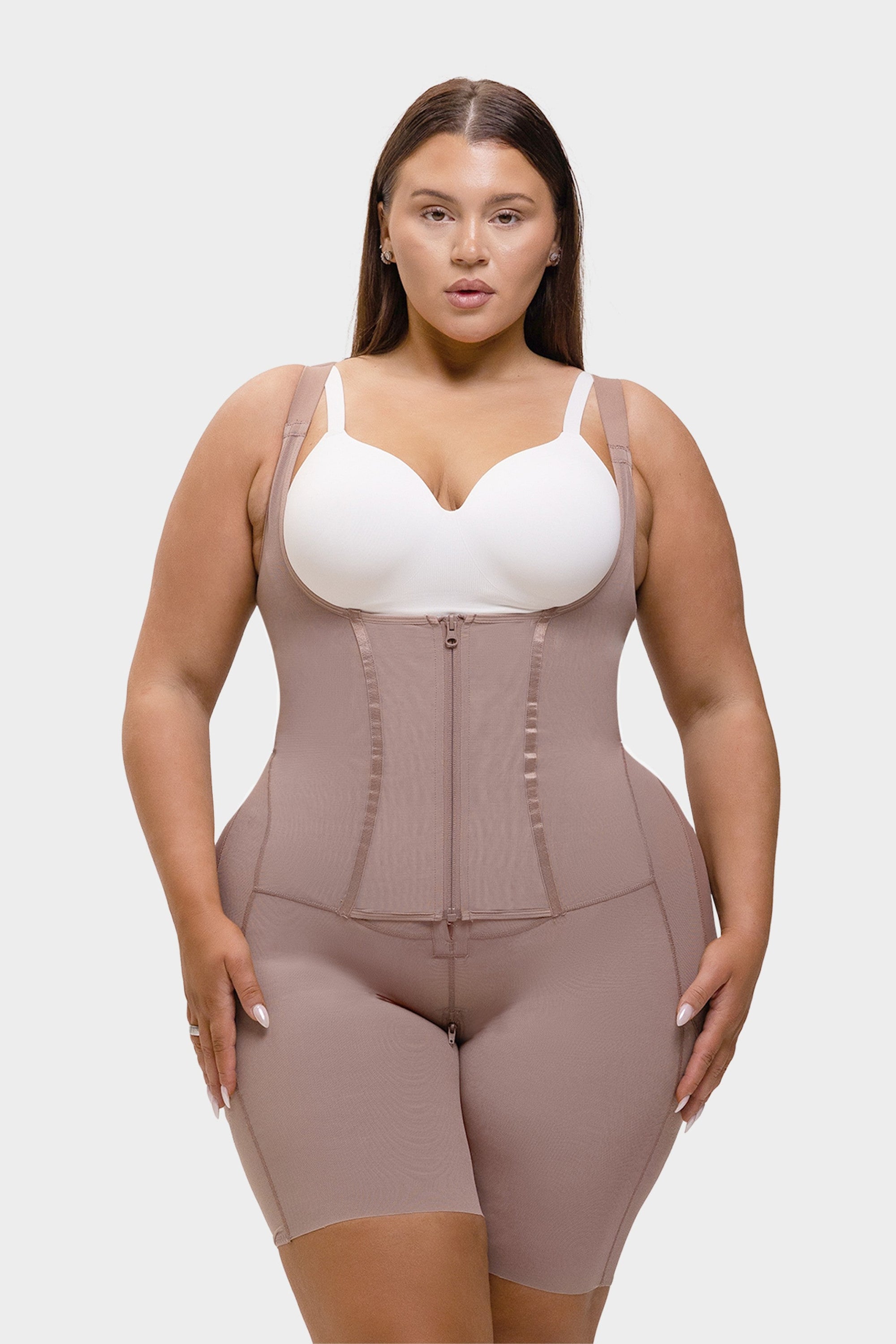 Woman wearing a beige waist trainer over a white top on a plain background