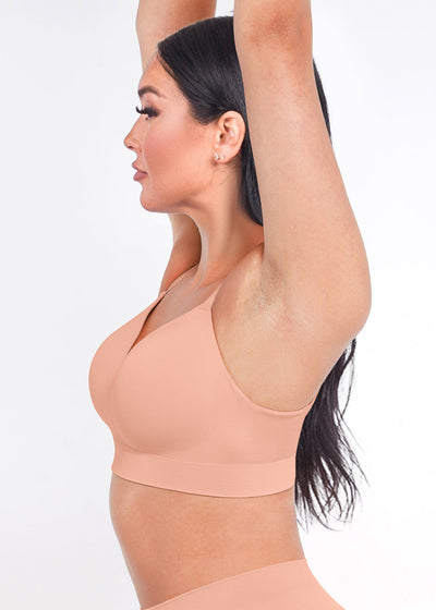 Woman wearing a peach-colored sports bra and leggings on a white background