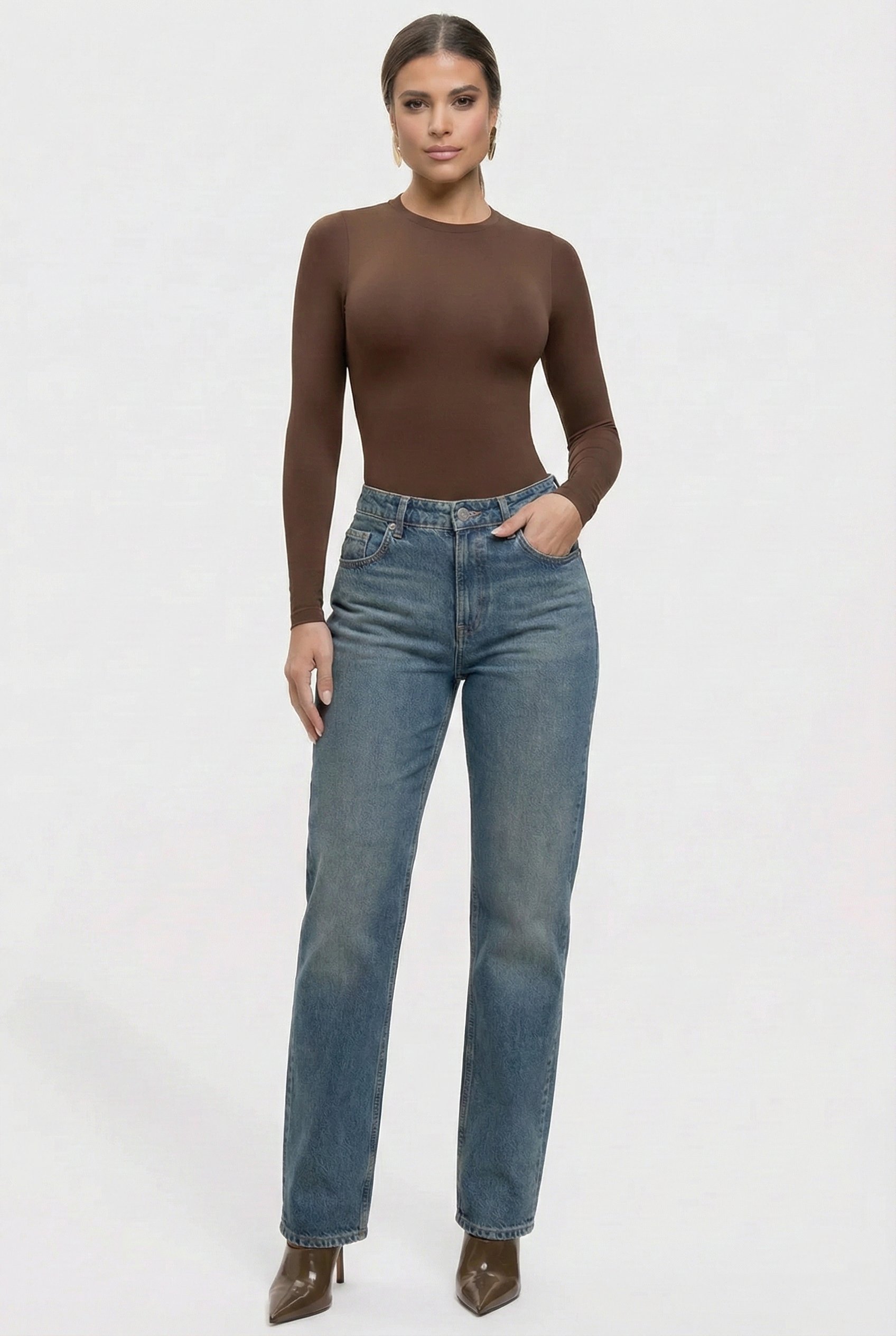 Woman wearing a brown long-sleeve top and blue jeans on a white background